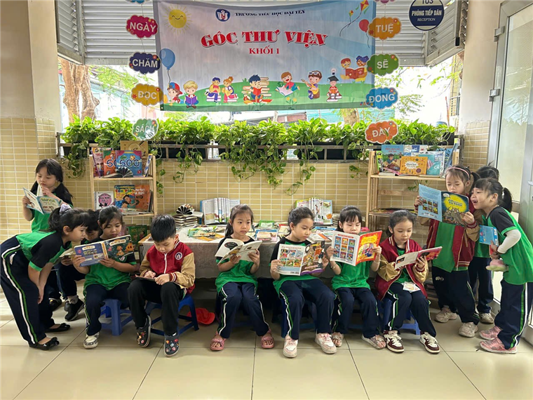 A group of children sitting on a table reading books
Description automatically generated